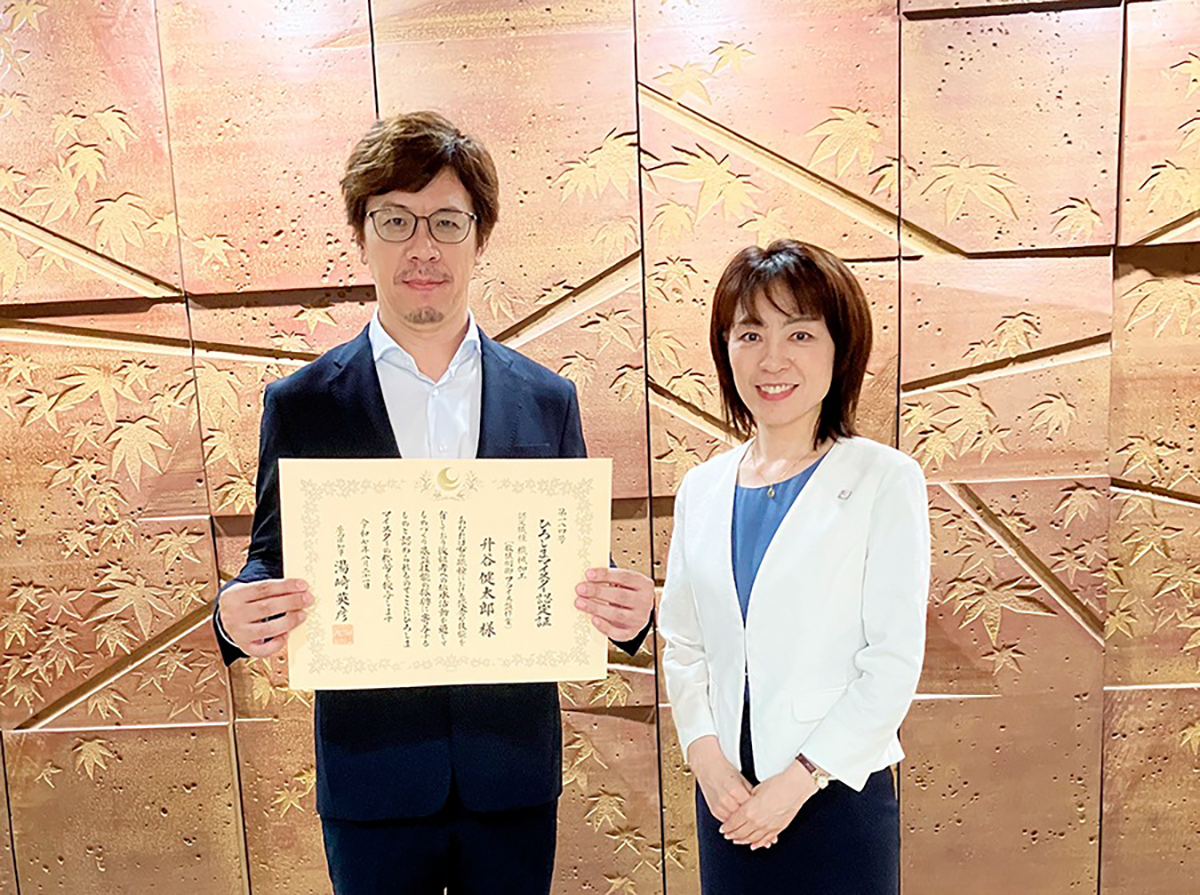 Masutani (left) smiling while holding his Meister certificate