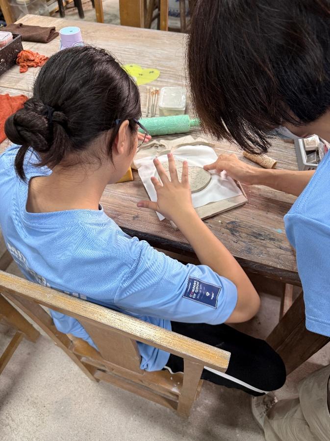 A participant shaping a pottery trinket dish with guidance from an MHI-ESA volunteer